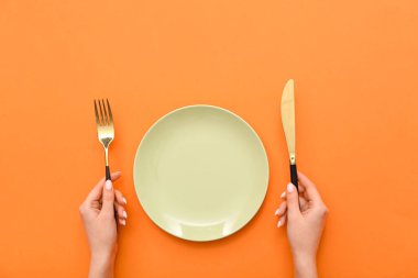 Çatal bıçaklı kadın elleri ve turuncu arka planda boş tabak.