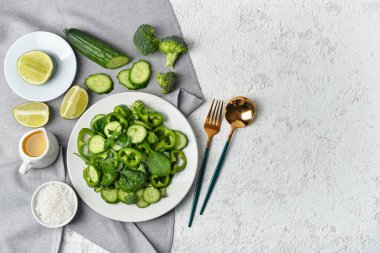 Yeşil sebzeli bir tabak salata ve arkaplanda malzemeler.