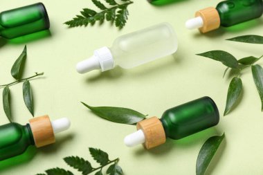 Açık yeşil arka planda bitki dalları olan kozmetik yağı şişeleri