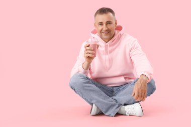Pembe arka planda oturmuş meyveli buzlu içecek içen olgun bir adam.