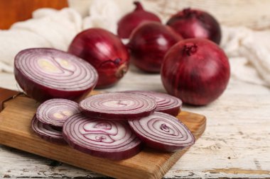 Beyaz ahşap zemin üzerinde taze kırmızı soğan dilimleri olan tahta.