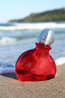 Okyanus kıyısındaki kumsalda bir şişe lüks parfüm, yakın plan.