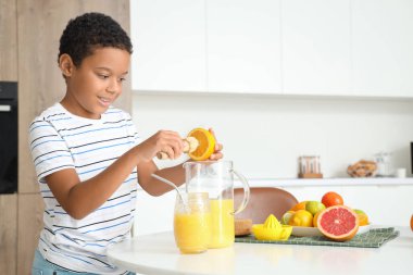 Küçük Afro-Amerikalı çocuk mutfaktaki masada taze narenciye suyu yapıyor.