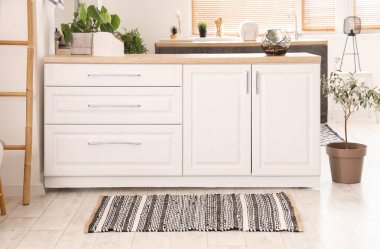 Beyaz tezgahlı ve çizgili halılı aydınlık mutfağın içi.