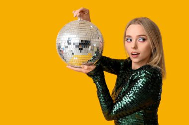 Sarı arka planda disko topu olan güzel genç bir kadın.
