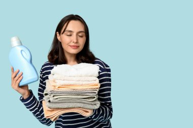 Temiz havluları ve mavi arka planda bir şişe deterjanı olan genç bir kadın.