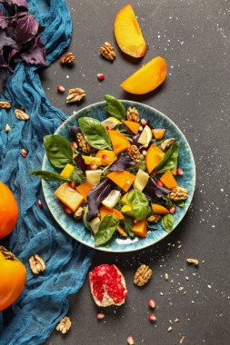 Bir tabak lezzetli salata, hurma, nar tohumu ve siyah arka planda ceviz.