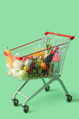 Yeşil arka planda farklı yiyeceklerle dolu alışveriş arabası.