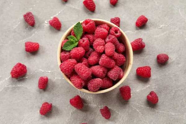 Gri arka planda taze ahududu ve naneli kase, yakın plan.