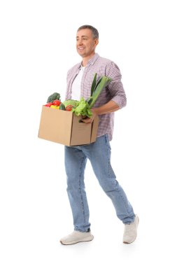 Beyaz arka planda yürüyen bir kutu taze sebzeli olgun bir adam.