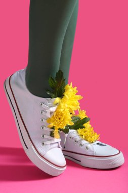Pembe arka planda sarı kasımpatı çiçekleri olan beyaz ayakkabılı güzel genç kadın bacakları.