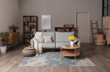 Interior of stylish living room with grey sofa, plaid, coffee table and flowers