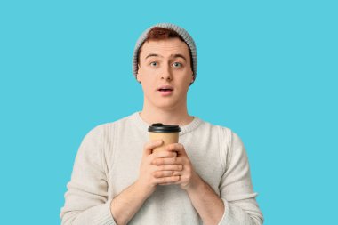 Şapkalı genç adam ve mavi arka planda bir fincan kahve.