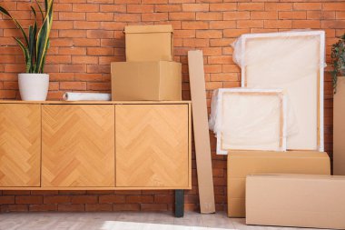 Mobilyalar, ev bitkisi ve karton kutular kahverengi tuğla duvarın yanında. Taşınma konsepti