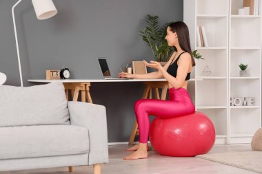 Evde spor yaparken dizüstü bilgisayar kullanan genç bir kadın.