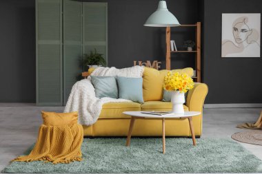 Sarı kanepe, ekoseler, çiçekli vazo ve oturma odasında kahve masası.