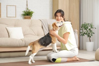 Oturma odasında yoga minderinde sevimli Beagle köpeği olan genç ve sportif bir kadın.