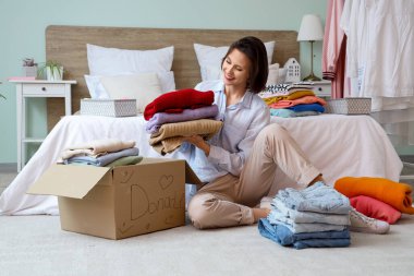 Genç ve güzel bir kadın, farklı kıyafetleri bağış kutusunda katlıyor.