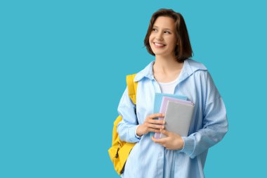 Sırt çantası ve mavi arka plan kitapları olan güzel bir kız öğrenci.