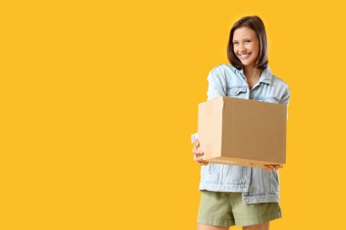 Sarı arka planda bir paket kutusu olan güzel, mutlu genç bir kadın.