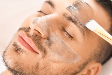 Güzellik uzmanı kaplıca salonunda yakışıklı adamın yüzüne kozmetik balon maskesi takıyor.