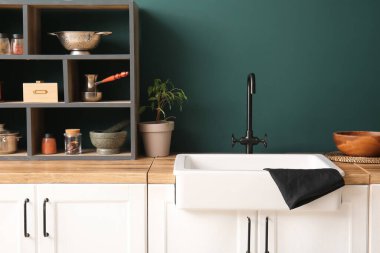 Beyaz seramik lavabo ve raf ünitesi mutfaktaki koyu mavi duvarın yanındaki ahşap tezgahın üzerinde.