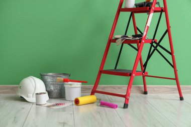 Yeşil duvarın yanında boya ve aletlerle dolu merdiven.