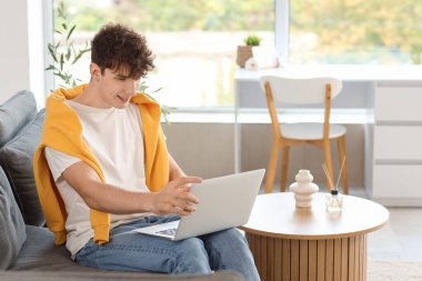 Genç adam evdeki kanepede dizüstü bilgisayarla görüntülü sohbet ediyor.