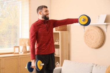 Sportif genç adam evde dambıllarla egzersiz yapıyor.