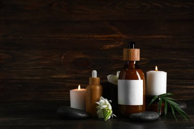 Kozmetik ürünleri, spa aksesuarları, yanan mumlar ve koyu ahşap arka planda çiçekler.