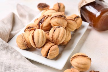 Beyaz arka planda kaynamış yoğunlaştırılmış sütle ceviz şeklinde kurabiyeler, yakın plan.