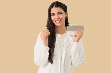 Bej arka planda diş rengi örnekleri olan kadın dişçi.