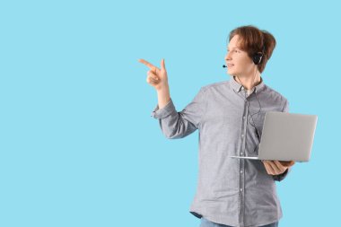 Dizüstü bilgisayarı ve kulaklığı olan genç bir çocuk mavi arka planda bir şeyi işaret ediyor. Serbest konsept