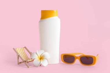 Dekoratif iskemle, Plumeria çiçeği, güneş gözlüğü ve pembe arka planda bir şişe güneş kremi ile kompozisyon