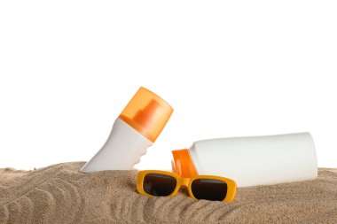 Güneş gözlüğü ve güneş kremi şişeleri beyaz arka planda kumun üzerinde