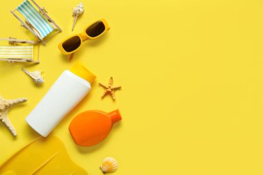 Paletlerle, güneş gözlükleriyle, deniz kabuklarıyla ve sarı arka planda güneş kremi şişeleriyle kompozisyon