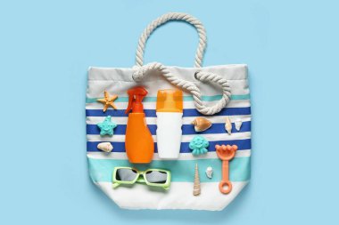 Çantalı, güneş gözlüklü, dekoratif deniz kabuklu, deniz yıldızlı ve mavi arka planda güneş kremi şişeli kompozisyon