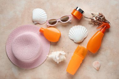 Bej rengi arka planda şapka, güneş gözlüğü, deniz kabuğu, kavanoz ve güneş kremi şişeleriyle kompozisyon
