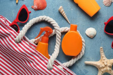 Çantalı kompozisyon, güneş kremi şişeleri, güneş gözlüğü, deniz yıldızı ve deniz kabukları mavi grunge arka planda