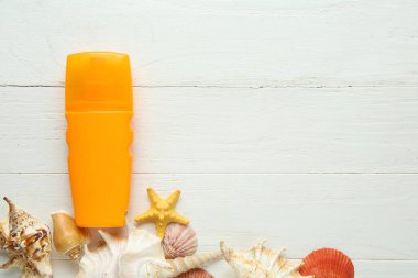 Beyaz ahşap arka planda güneş kremi, deniz kabuğu ve deniz yıldızı karışımı.
