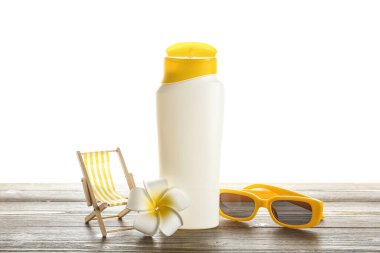 Güneş gözlüğü, dekoratif iskemle, bir şişe güneş kremi ve ahşap masada beyaz arka planda bir çiçek.