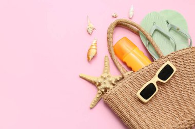 Deniz yıldızları, deniz kabukları, bir şişe güneş kremi ve pembe arka planda plaj aksesuarları.