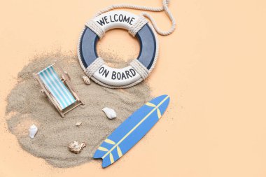 Kumlu kompozisyon, dekoratif iskemle, bej arka planda sörf tahtası ve can simidi.