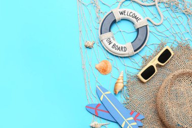 Deniz kabukları, ağ, şapka, güneş gözlüğü, dekoratif sörf tahtaları ve mavi arka planda can simidi olan kompozisyon