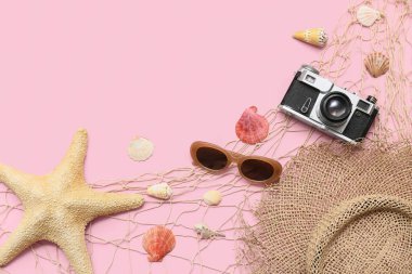 Kabuklu kompozisyon, fotoğraf makinesi, ağ ve pembe arka planda plaj aksesuarları.