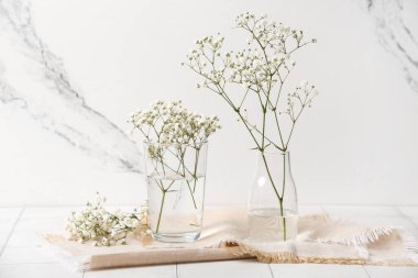 Mermer duvarın yanındaki beyaz döşeme masasında güzel çingene çiçekleri olan cam vazolar.