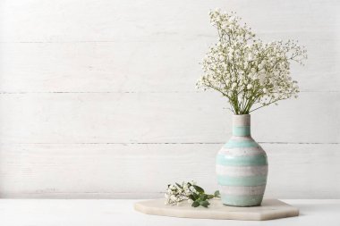 Beyaz ahşap arka planda güzel çingene çiçekleriyle tepsi ve vazo.