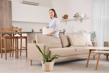 Oturma odasında dizüstü bilgisayarıyla kanepede oturan güzel genç bir kadın.