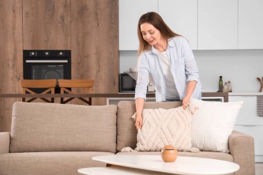 Güzel genç bir kadın, oturma odasındaki koltukta yastığı ayarlıyor.