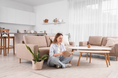 Genç ve güzel bir kadın oturma odasında oturmuş kitap okuyor.